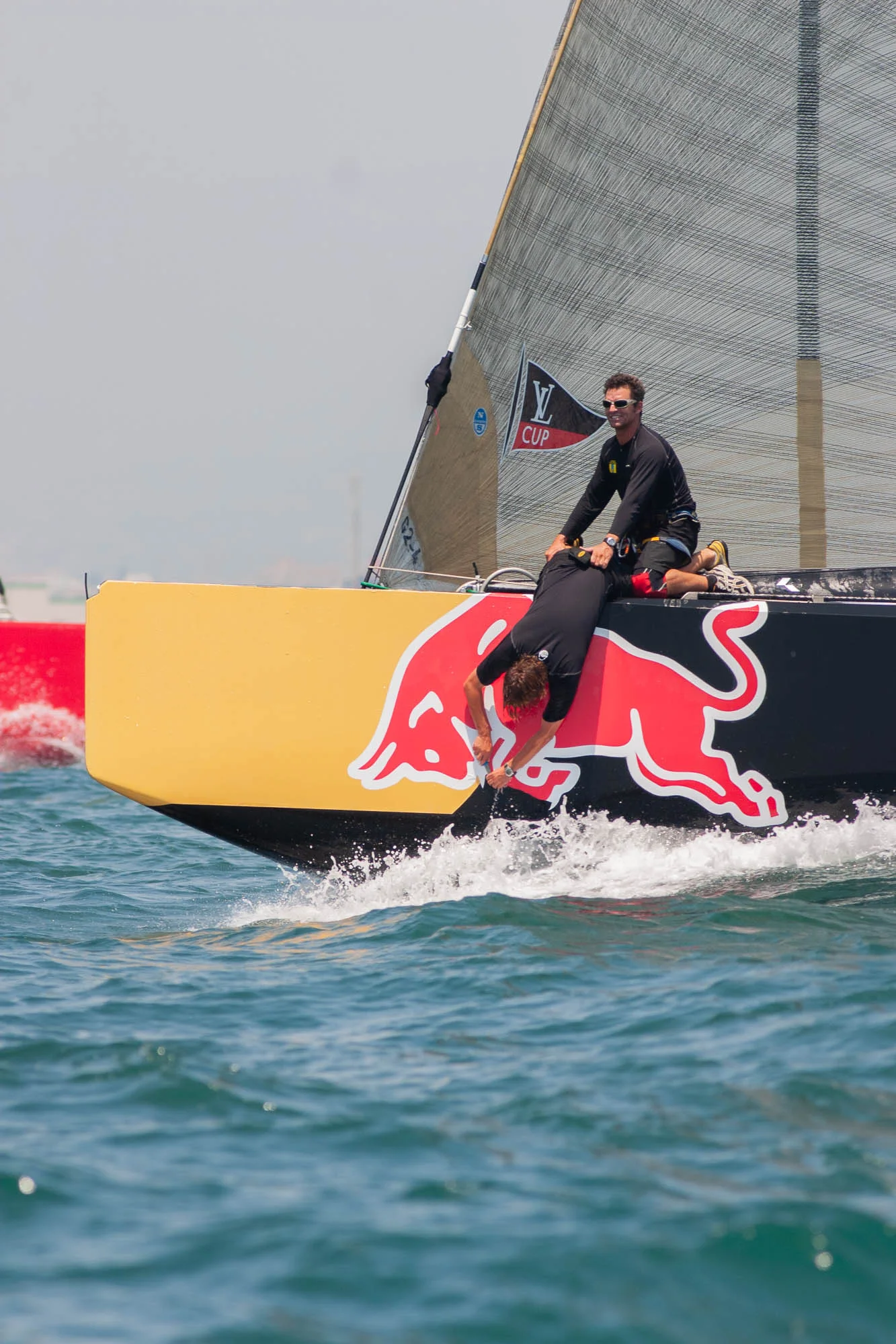 Velisti a prua di una barca da regata gialla e nera con il logo Red Bull