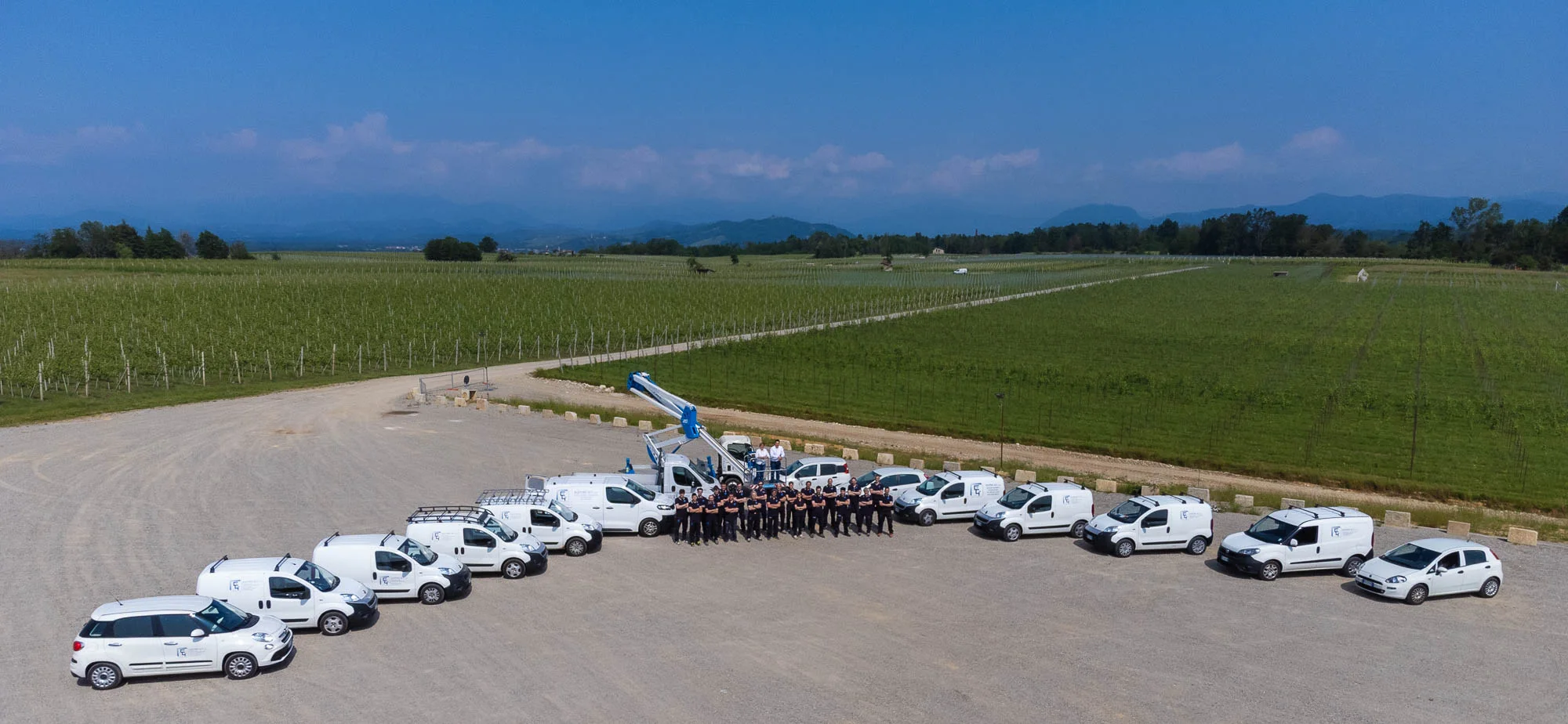 Furgoni e auto aziendali disposti a semicerchio con i dipendenti al centro, vista dal drone