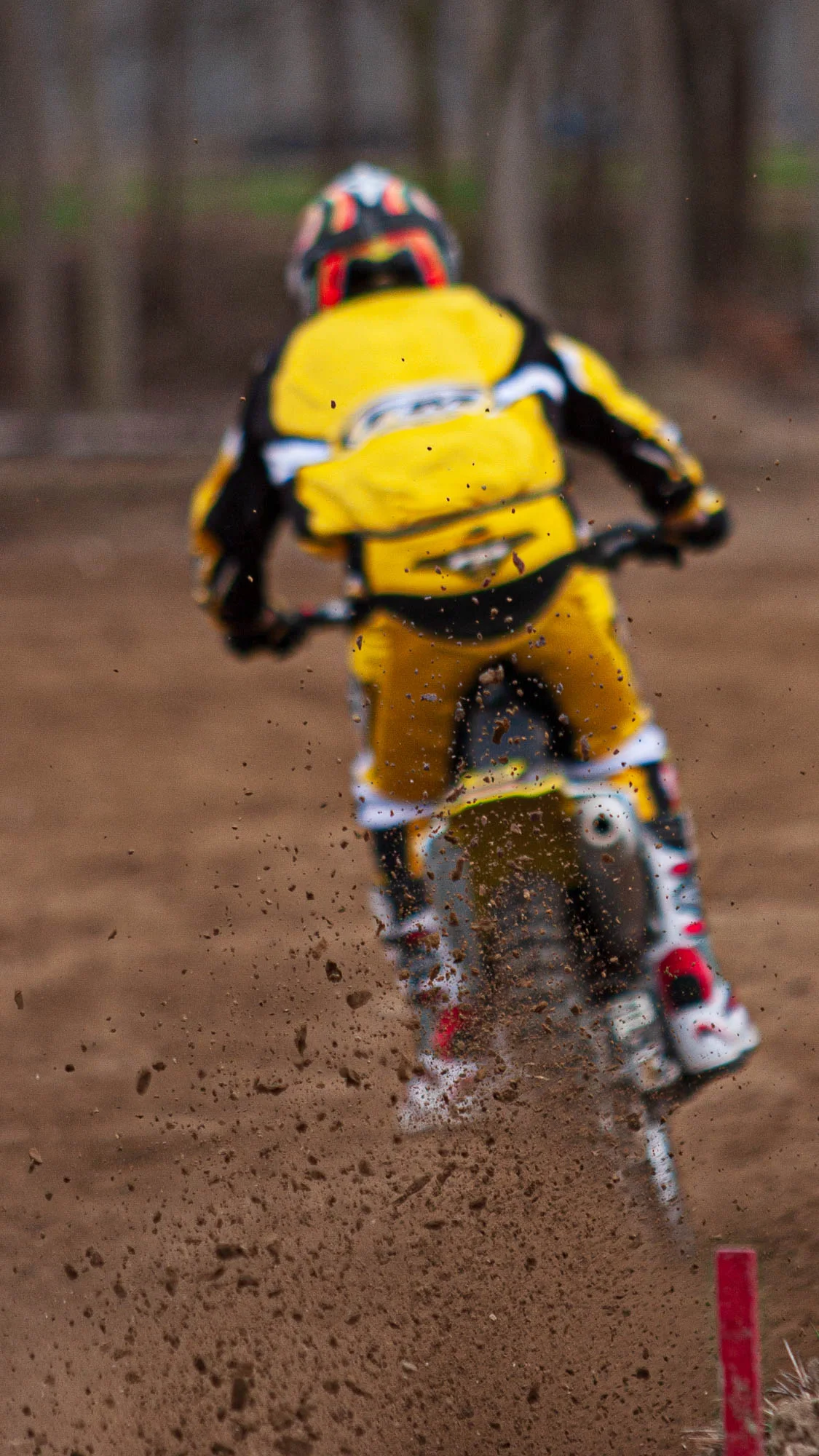 Pilota di motocross in tuta gialla visto da dietro mentre solleva la terra