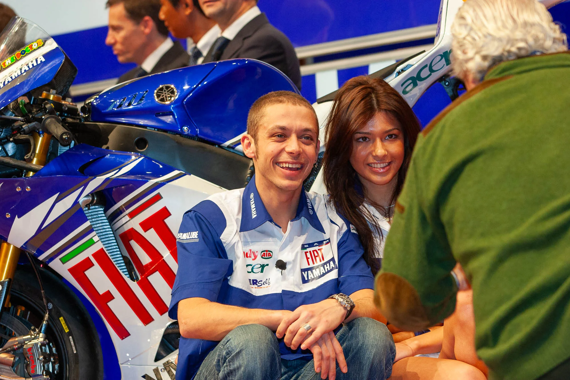 Valentino Rossi ride seduto accanto alla sua moto durante la presentazione, mentre Gigi Soldano lo fotografa