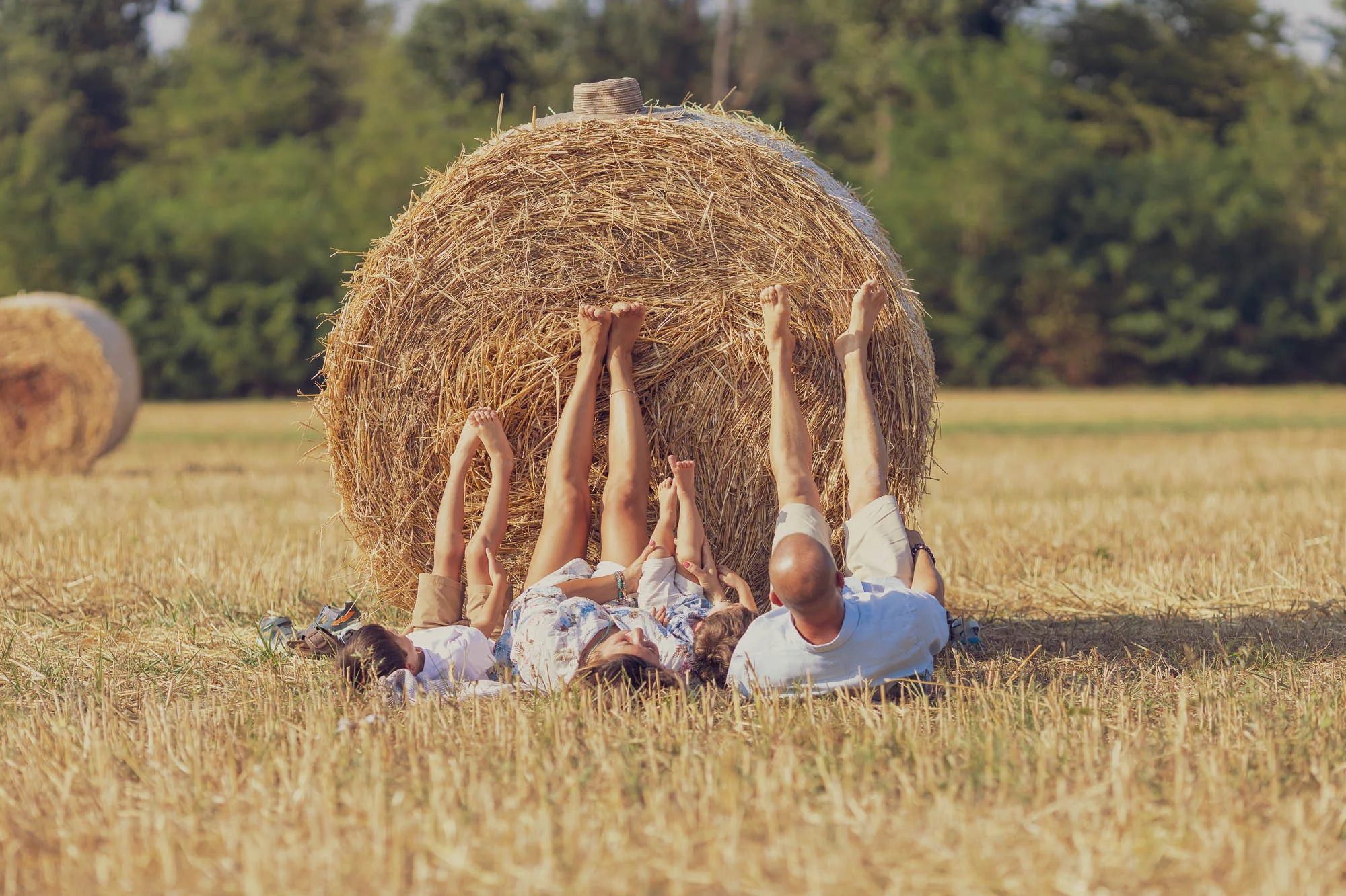 Famiglia sdraiata sul prato con le gambe alzate appoggiate a una balla di fieno